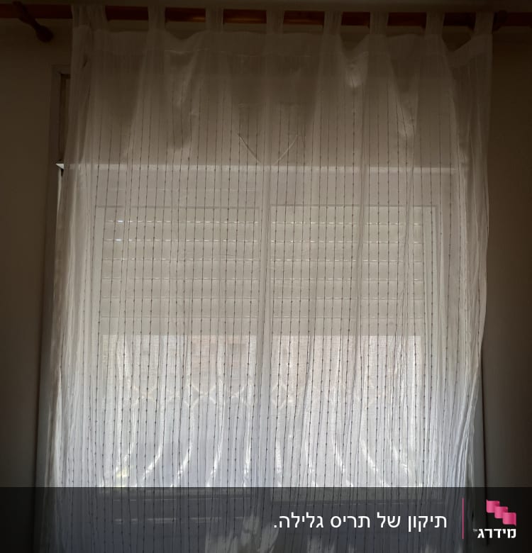 תריסים סגורים מאחורי וילון לבן שקוף